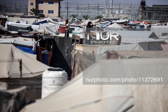 Palestinians are walking along an alley between tents sheltering displaced Palestinians in Rafah in the southern Gaza Strip on June 30, 2024...