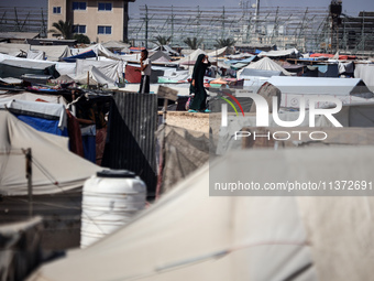 Palestinians are walking along an alley between tents sheltering displaced Palestinians in Rafah in the southern Gaza Strip on June 30, 2024...