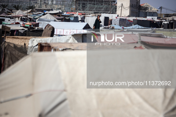 Palestinians are walking along an alley between tents sheltering displaced Palestinians in Rafah in the southern Gaza Strip on June 30, 2024...