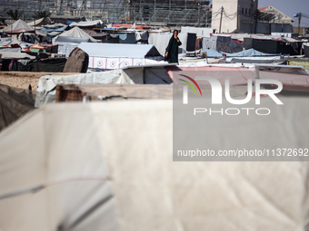 Palestinians are walking along an alley between tents sheltering displaced Palestinians in Rafah in the southern Gaza Strip on June 30, 2024...