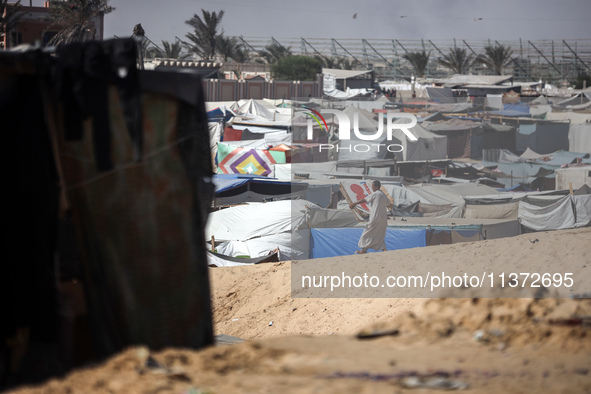 Palestinians are walking along an alley between tents sheltering displaced Palestinians in Rafah in the southern Gaza Strip on June 30, 2024...