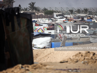 Palestinians are walking along an alley between tents sheltering displaced Palestinians in Rafah in the southern Gaza Strip on June 30, 2024...