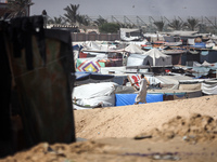 Palestinians are walking along an alley between tents sheltering displaced Palestinians in Rafah in the southern Gaza Strip on June 30, 2024...