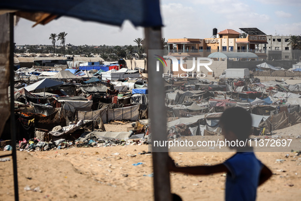 Palestinians are walking along an alley between tents sheltering displaced Palestinians in Rafah in the southern Gaza Strip on June 30, 2024...