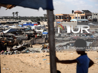 Palestinians are walking along an alley between tents sheltering displaced Palestinians in Rafah in the southern Gaza Strip on June 30, 2024...