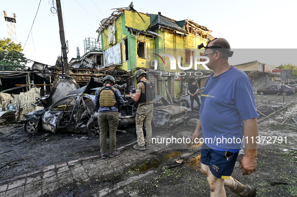 A man is walking past criminal experts who are examining cars destroyed by the Russian missile strike in central Vilniansk, Zaporizhzhia reg...