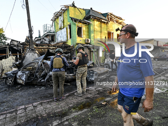 A man is walking past criminal experts who are examining cars destroyed by the Russian missile strike in central Vilniansk, Zaporizhzhia reg...