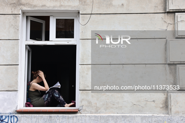 A reading person sits at a window in Krakow, Poland on June 30, 2024. 