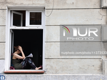 A reading person sits at a window in Krakow, Poland on June 30, 2024. (