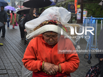 An old woman is carrying a heavy load during rainfall in Darjeeling, India, on July 1, 2024. Darjeeling is a famous tourist destination in N...