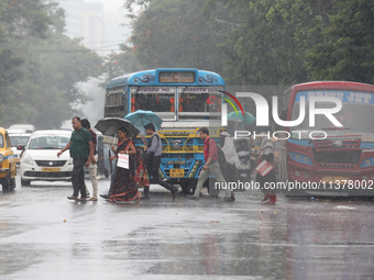 Commuters are crossing a busy road with umbrellas during monsoon rain in Kolkata, India, on July 2, 2024. (