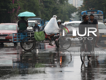 A man is sitting with an umbrella as another man is covering himself with a plastic sheet while paddling his rickshaw on a busy road during...