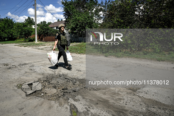 A police officer is carrying bags with humanitarian aid past a hole in the road from a Russian projectile in the rural settlement of Stepnoh...