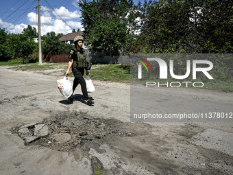 A police officer is carrying bags with humanitarian aid past a hole in the road from a Russian projectile in the rural settlement of Stepnoh...