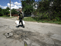 A police officer is carrying bags with humanitarian aid past a hole in the road from a Russian projectile in the rural settlement of Stepnoh...