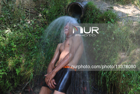 A Kashmiri boy is cooling off under an overflowing water pipe during a hot day on the outskirts of Srinagar, Jammu And Kashmir, on July 2, 2...