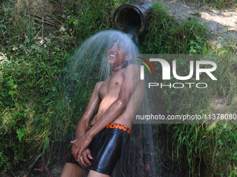 A Kashmiri boy is cooling off under an overflowing water pipe during a hot day on the outskirts of Srinagar, Jammu And Kashmir, on July 2, 2...