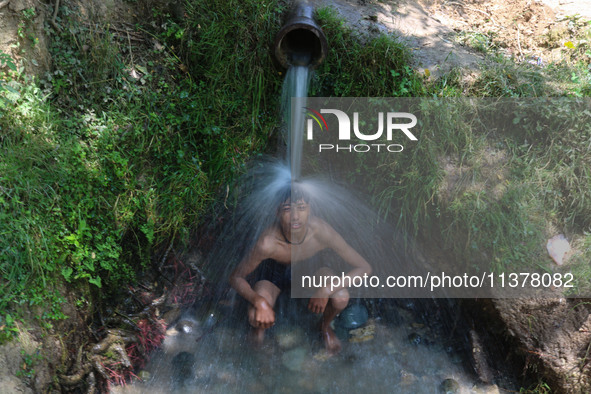 A Kashmiri boy is cooling off under an overflowing water pipe during a hot day on the outskirts of Srinagar, Jammu And Kashmir, on July 2, 2...