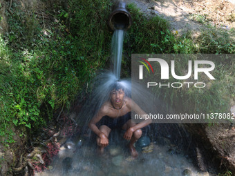 A Kashmiri boy is cooling off under an overflowing water pipe during a hot day on the outskirts of Srinagar, Jammu And Kashmir, on July 2, 2...