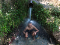 A Kashmiri boy is cooling off under an overflowing water pipe during a hot day on the outskirts of Srinagar, Jammu And Kashmir, on July 2, 2...