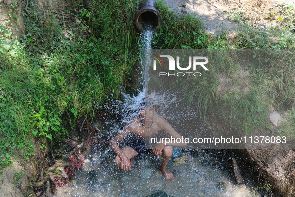 A Kashmiri boy is cooling off under an overflowing water pipe during a hot day on the outskirts of Srinagar, Jammu And Kashmir, on July 2, 2...