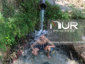 A Kashmiri boy is cooling off under an overflowing water pipe during a hot day on the outskirts of Srinagar, Jammu And Kashmir, on July 2, 2...