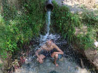 A Kashmiri boy is cooling off under an overflowing water pipe during a hot day on the outskirts of Srinagar, Jammu And Kashmir, on July 2, 2...