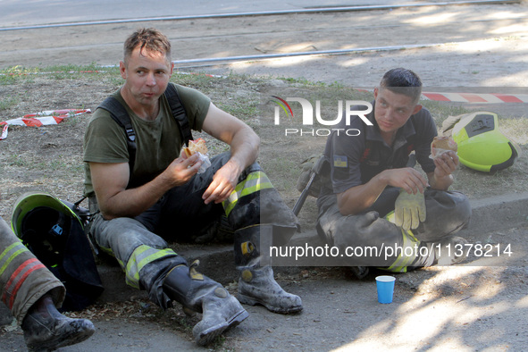 Rescuers are eating during a break as a response effort is underway at the apartment block hit by a Russian missile in Dnipro, Ukraine, on J...