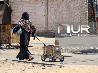 A Palestinian woman is walking in the street and dragging her son in Deir el-Balah, in the central Gaza Strip, on July 2, 2024, amid the ong...