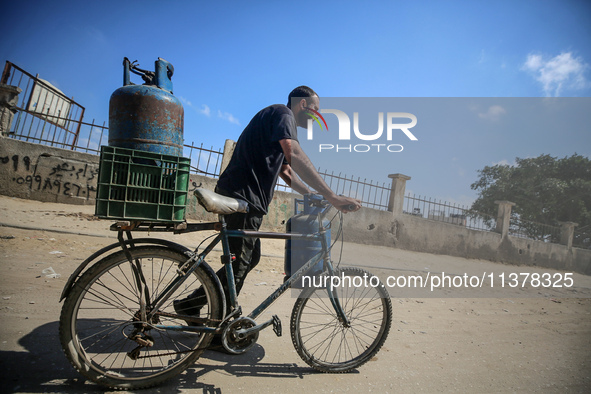 A Palestinian man is riding a bicycle carrying a gas canister in Deir el-Balah in the central Gaza Strip on July 2, 2024, amid the ongoing c...