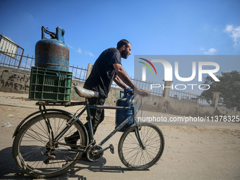 A Palestinian man is riding a bicycle carrying a gas canister in Deir el-Balah in the central Gaza Strip on July 2, 2024, amid the ongoing c...