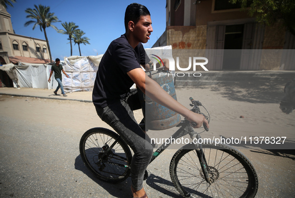 A Palestinian man is riding a bicycle carrying a gas canister in Deir el-Balah in the central Gaza Strip on July 2, 2024, amid the ongoing c...