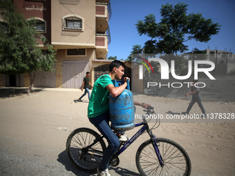 A Palestinian man is riding a bicycle carrying a gas canister in Deir el-Balah in the central Gaza Strip on July 2, 2024, amid the ongoing c...