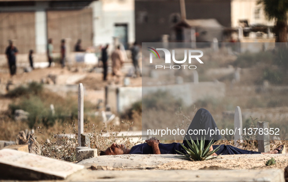 A man is sleeping next to tombstones and grave markers at a cemetery in Deir el-Balah in the central Gaza Strip on July 2, 2024, amid the on...