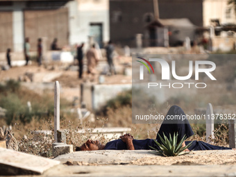 A man is sleeping next to tombstones and grave markers at a cemetery in Deir el-Balah in the central Gaza Strip on July 2, 2024, amid the on...