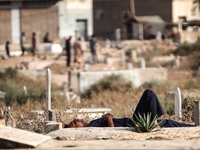 A man is sleeping next to tombstones and grave markers at a cemetery in Deir el-Balah in the central Gaza Strip on July 2, 2024, amid the on...