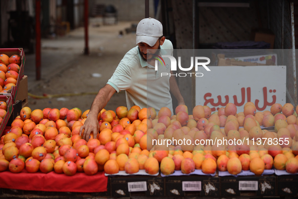 A produce merchant is arranging mangoes for sale at a stall along a market street in Deir el-Balah in the central Gaza Strip on July 2, 2024...