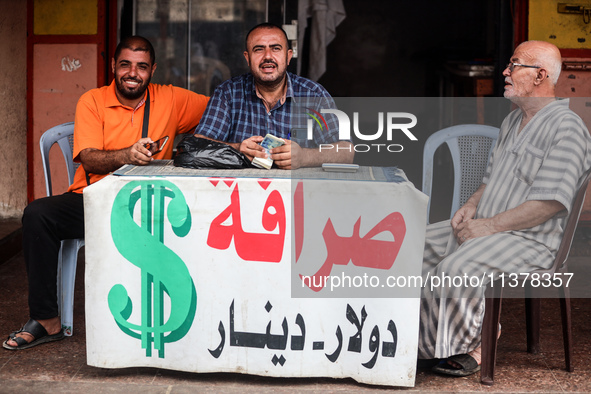 A man is counting stacks of Israeli shekel banknotes at an informal money exchange stall in Deir el-Balah in the central Gaza Strip on July...