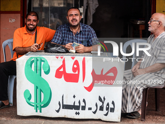 A man is counting stacks of Israeli shekel banknotes at an informal money exchange stall in Deir el-Balah in the central Gaza Strip on July...