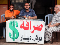 A man is counting stacks of Israeli shekel banknotes at an informal money exchange stall in Deir el-Balah in the central Gaza Strip on July...