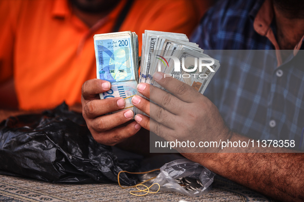 A man is counting stacks of Israeli shekel banknotes at an informal money exchange stall in Deir el-Balah in the central Gaza Strip on July...