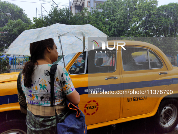 A woman is holding an umbrella, standing on the street, and waiting for buses during the rainy season in Kolkata, India, on July 2, 2024. 