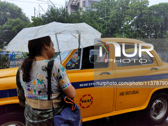 A woman is holding an umbrella, standing on the street, and waiting for buses during the rainy season in Kolkata, India, on July 2, 2024. (