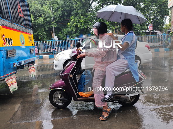 People are riding on a scooter in rainy weather in Kolkata, India, on July 2, 2024. 