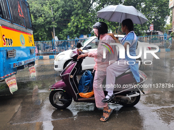 People are riding on a scooter in rainy weather in Kolkata, India, on July 2, 2024. (