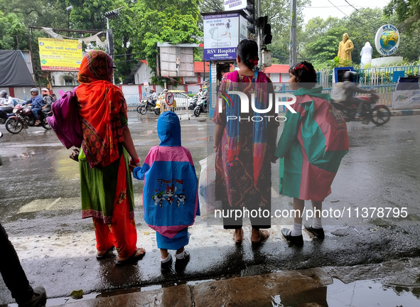 Women with their children are waiting beside the road to cross in rainy weather in Kolkata, India, on July 2, 2024. 