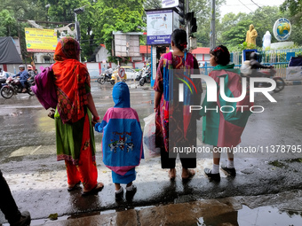 Women with their children are waiting beside the road to cross in rainy weather in Kolkata, India, on July 2, 2024. (