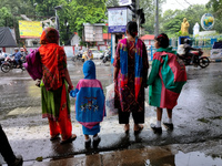 Women with their children are waiting beside the road to cross in rainy weather in Kolkata, India, on July 2, 2024. (