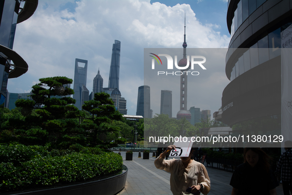 A woman is using an envelope to block the sun during the heatwave in Shanghai, China, on July 3, 2024. 