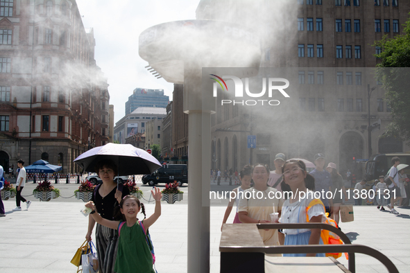 People are trying to reach the mist sprinkler during the heatwave at the Bund in Shanghai, China, on July 3, 2024. 